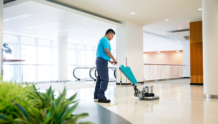 Two professional cleaners in navy aprons vacuuming floors and wiping walls during an apartment turnover cleaning service in Phoenix, AZ