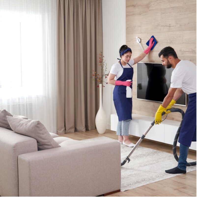Two professional cleaners in navy aprons vacuuming floors and wiping walls during an apartment turnover cleaning service in Phoenix, AZ.